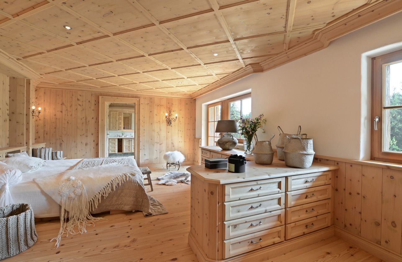 Cozy wood-paneled bedroom with twin beds, dresser, potted plants, and large windows