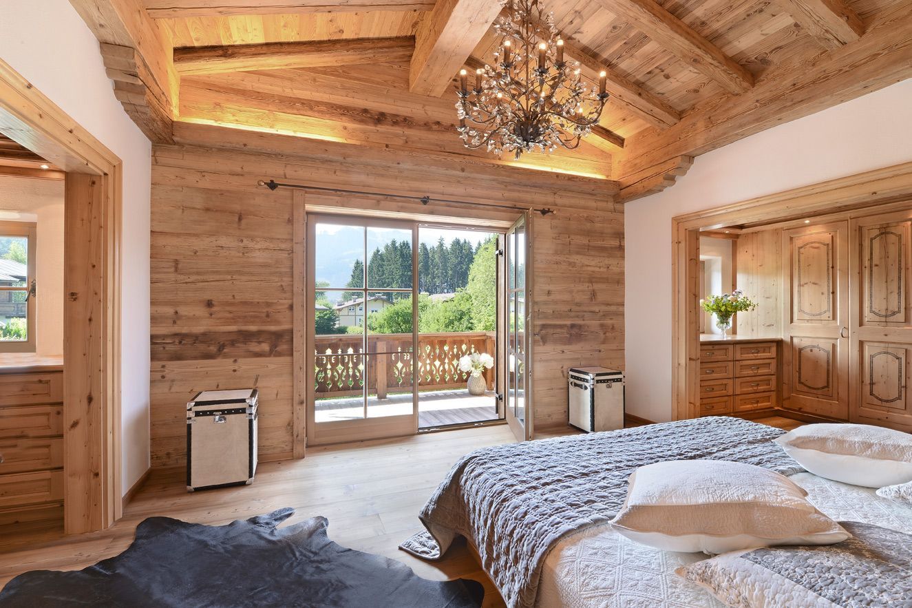 Cozy wooden bedroom with vaulted ceiling, large glass doors, and a balcony view of trees.