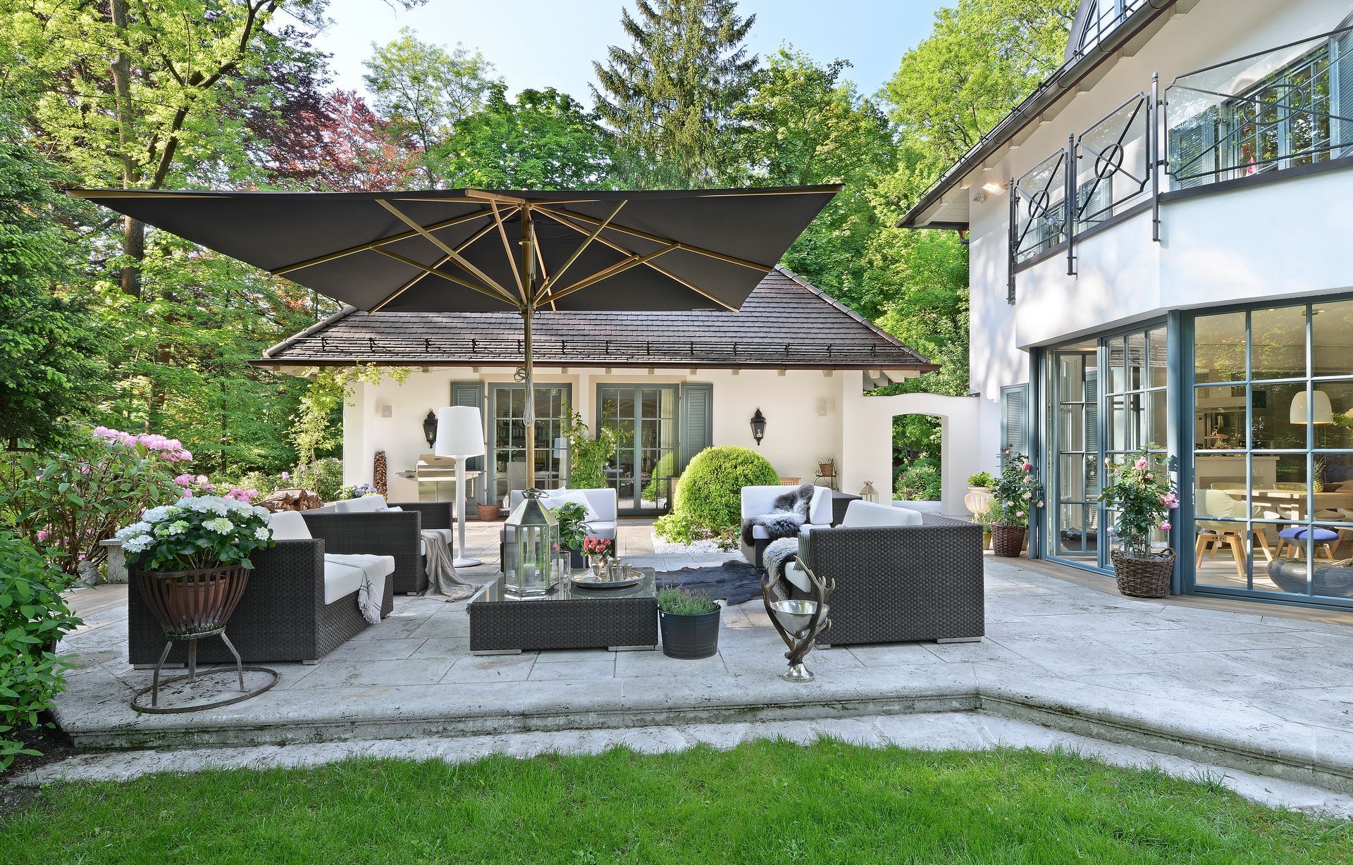 Patio seating area with black umbrellas, wicker chairs, and a house with large windows in the background