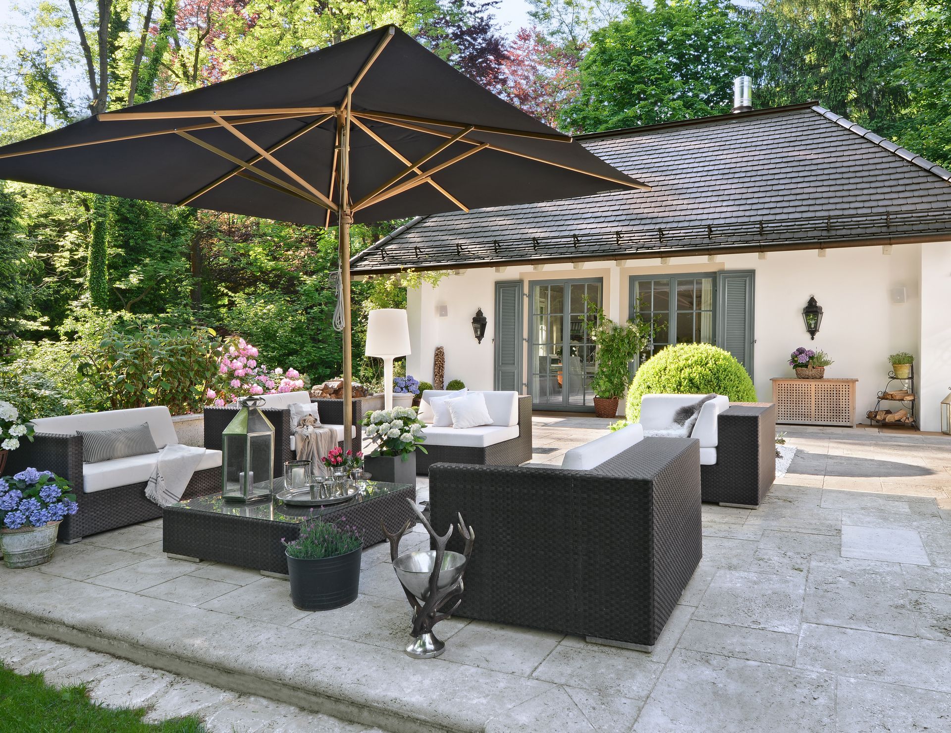 Stylish patio with wicker seating, black umbrellas, and a cream house in a lush garden