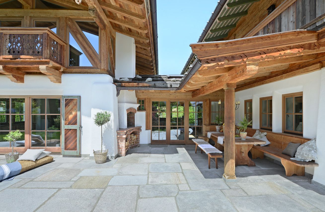 Stone courtyard with wooden beams, benches, and large windows in a rustic alpine-style house