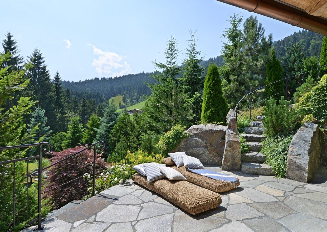 Outdoor stone patio with cushions and pillows overlooking a lush forested mountain view