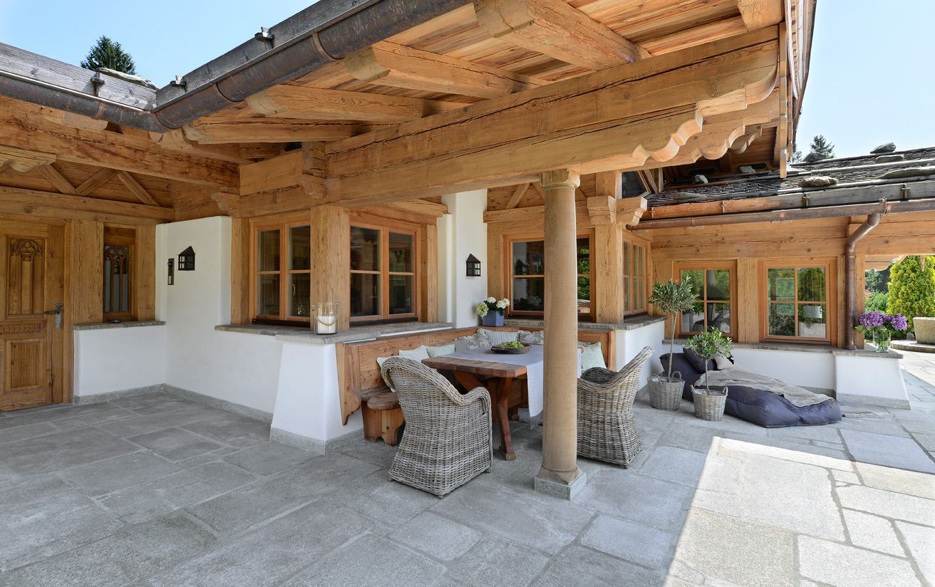 Rustic outdoor patio with wooden beams, stone tables, and lounge seating under a covered terrace.