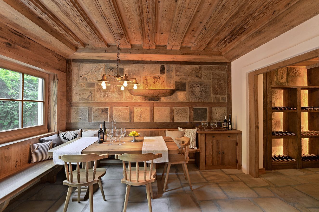 Rustic dining room with wood-paneled ceiling, long table, chairs, and window seat seating area