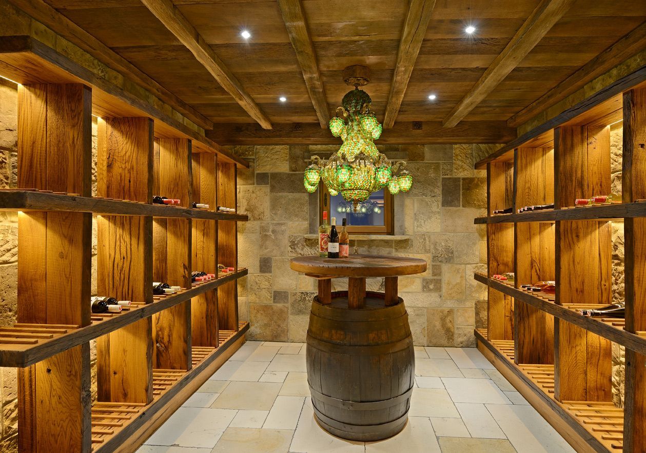 Wood-paneled wine cellar with barrel tables, shelves of bottles, and hanging greenery under warm lighting