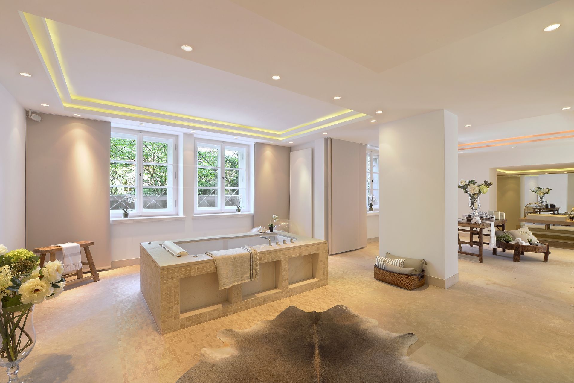 Bright modern living room with large windows, beige furniture, and warm recessed lighting.