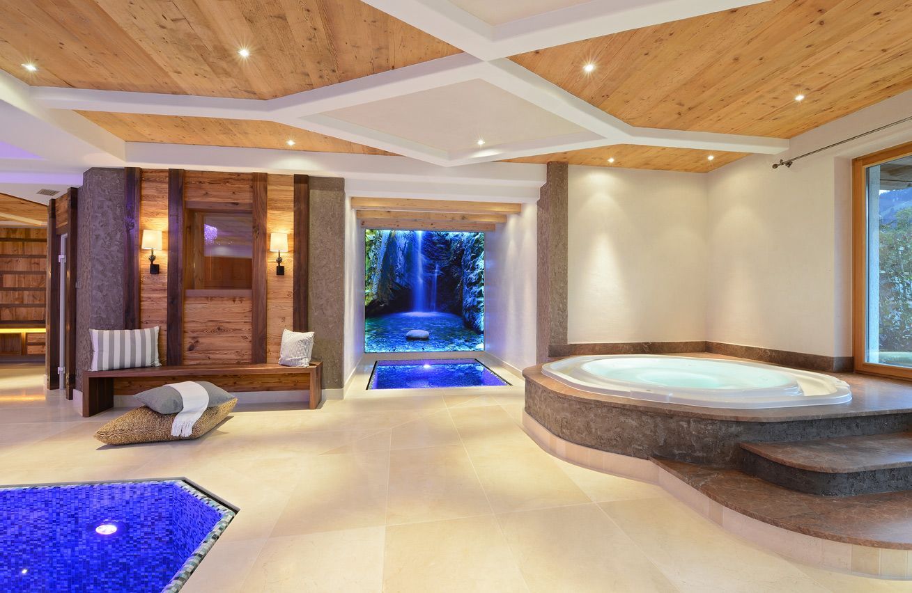 Luxury spa with indoor hot tub, blue-lit waterfall, wooden ceiling, and seating area