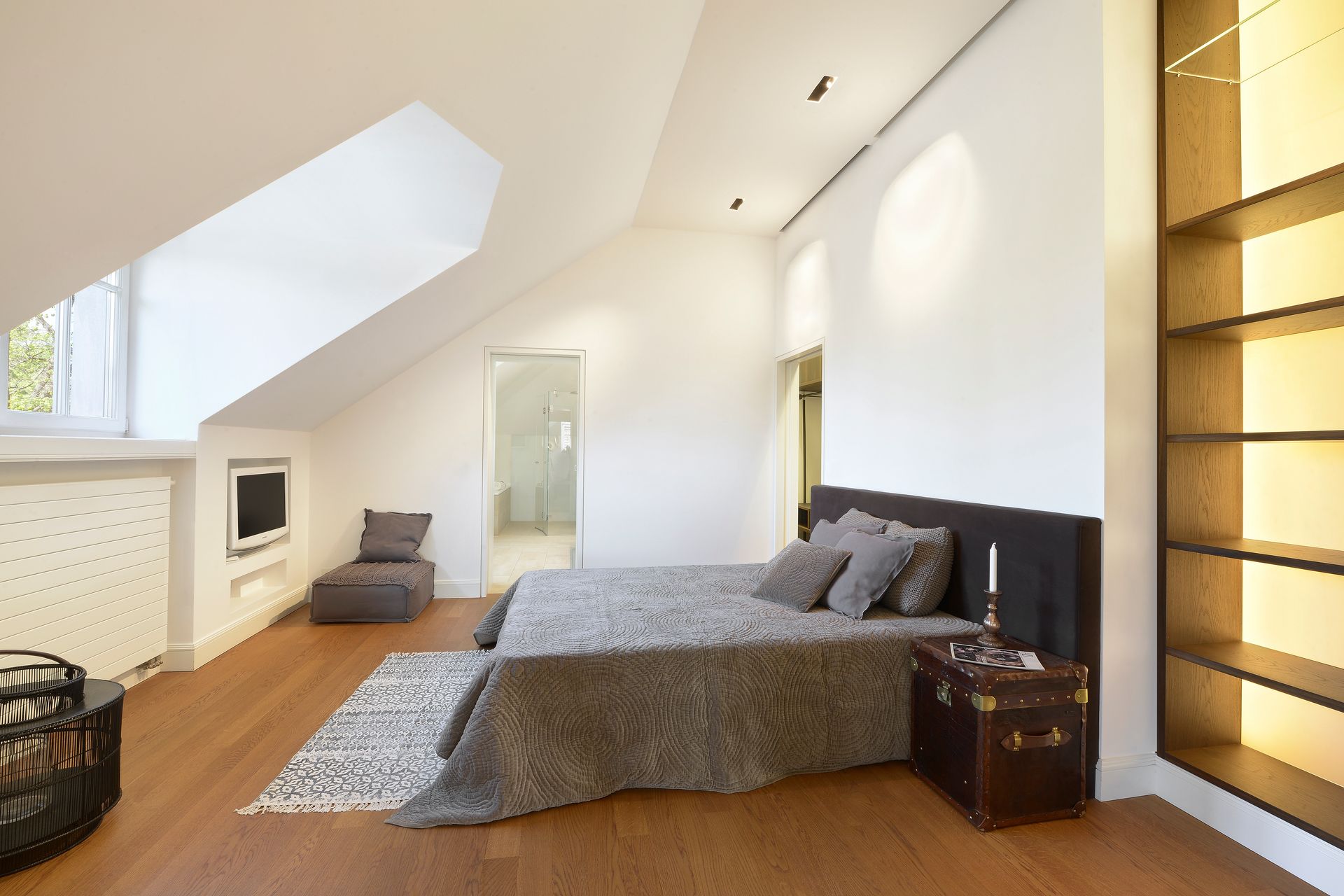 Bright modern bedroom with a skylight, sloped ceiling, gray bed, and wood flooring.