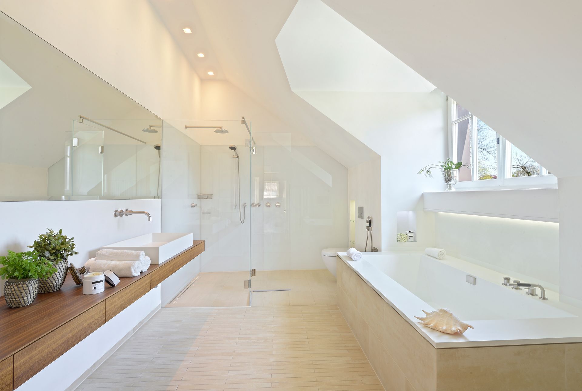 Bright modern bathroom with a tub, double sink, skylight, and light wood accents