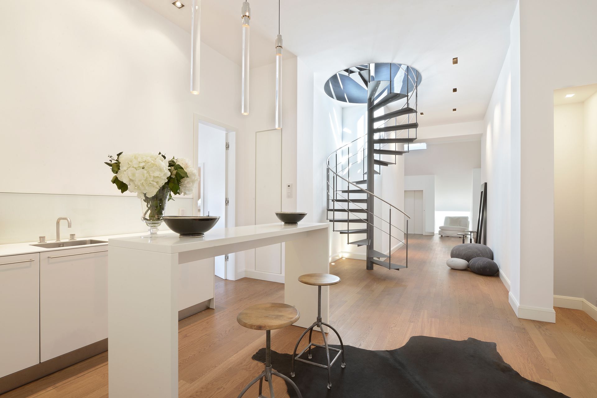 Modern white kitchen and living space with spiral staircase and wood floors