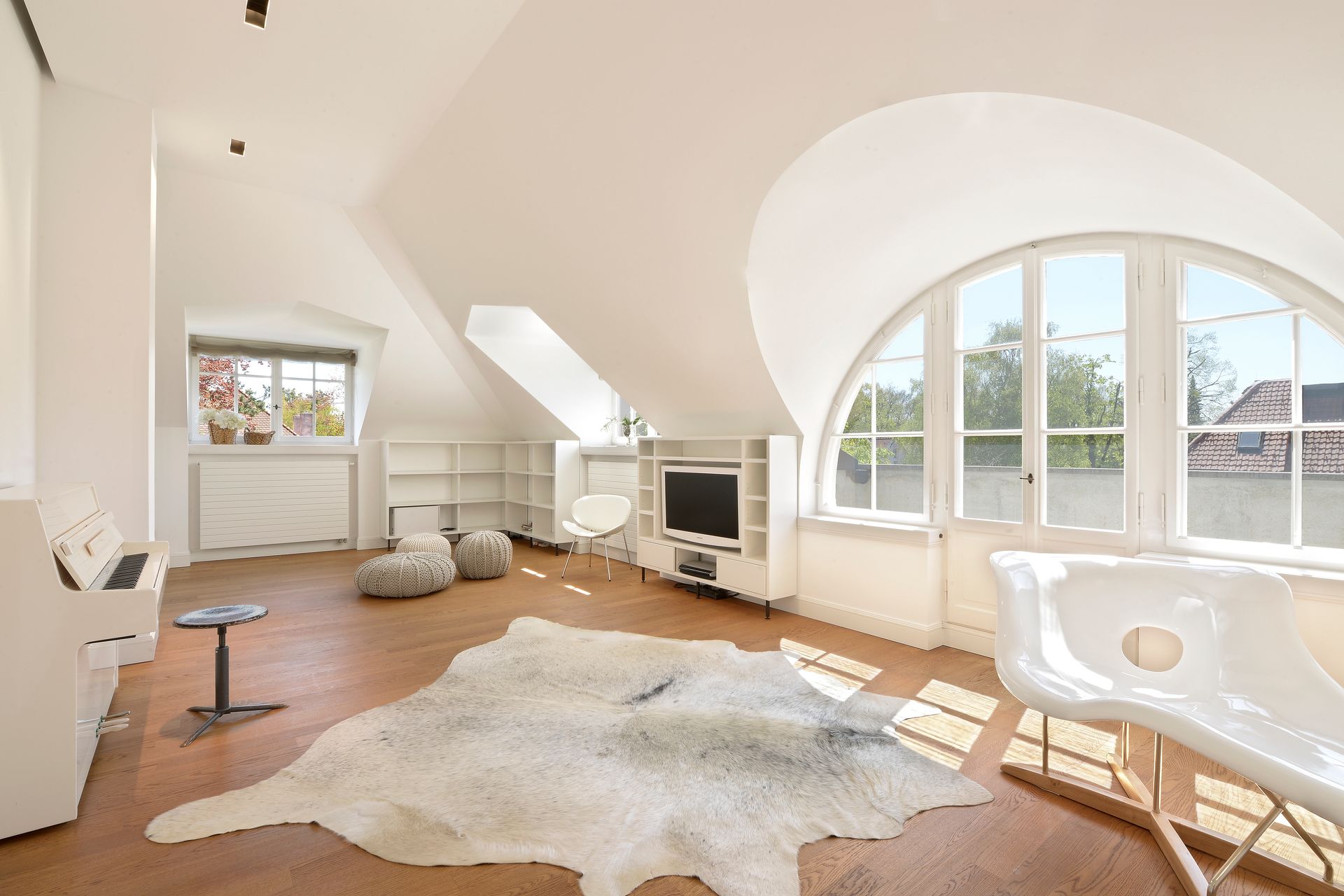 Bright attic living room with arched windows, white walls, wooden floor, and a shag rug.