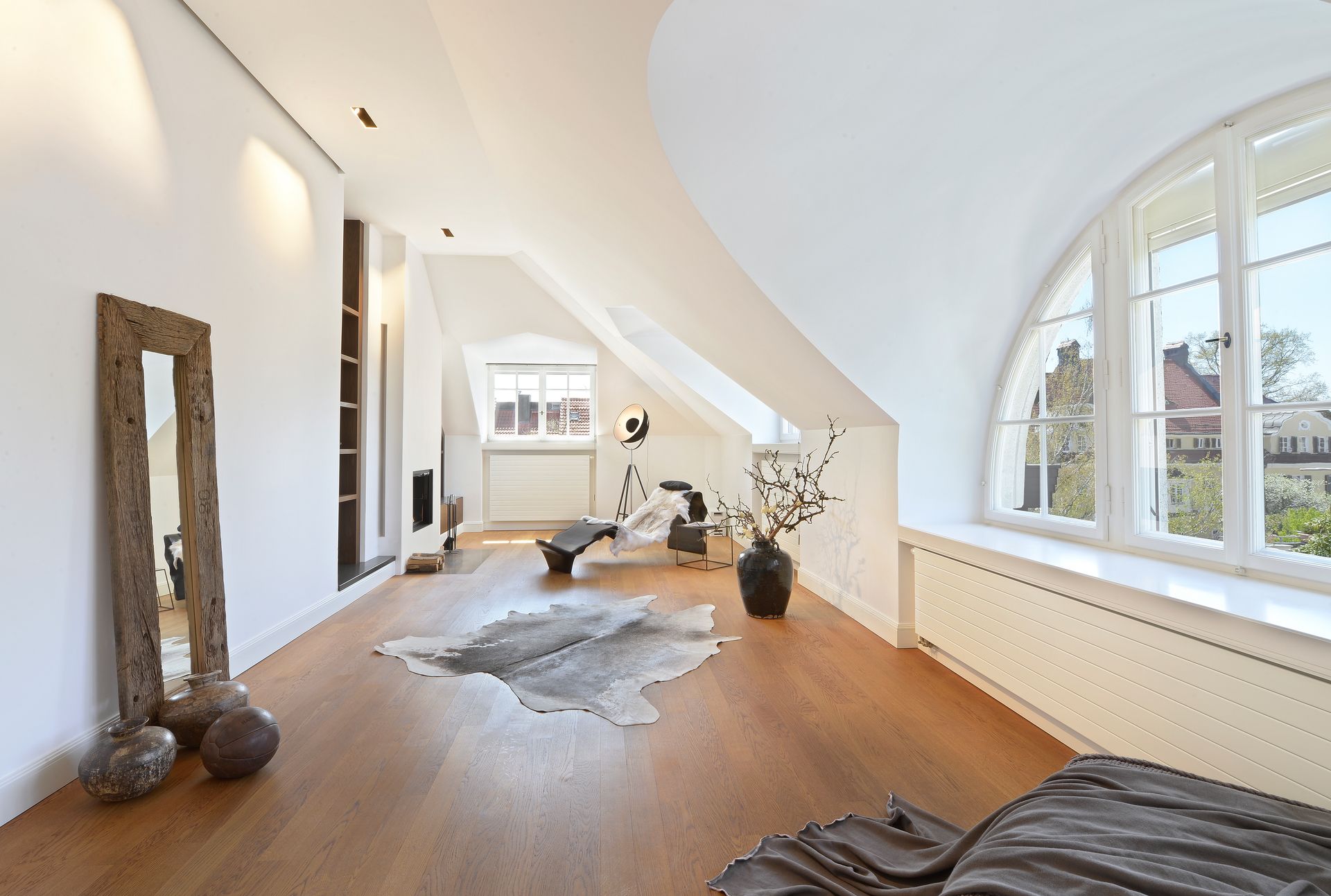 Bright, modern living room with curved ceiling, large arched window, and wooden floors.