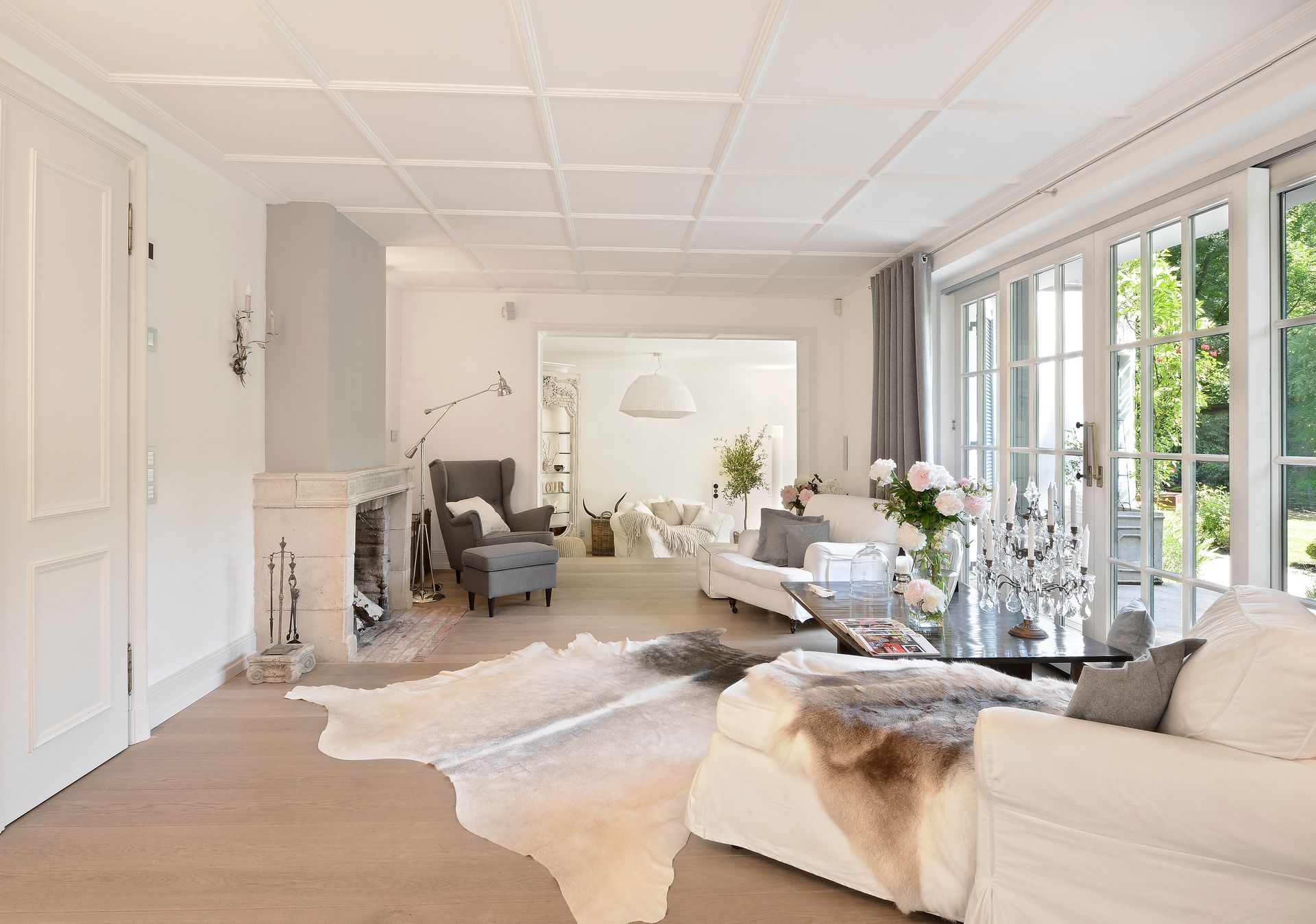 Bright modern living room with white sofas, large windows, neutral decor, and a fireplace.