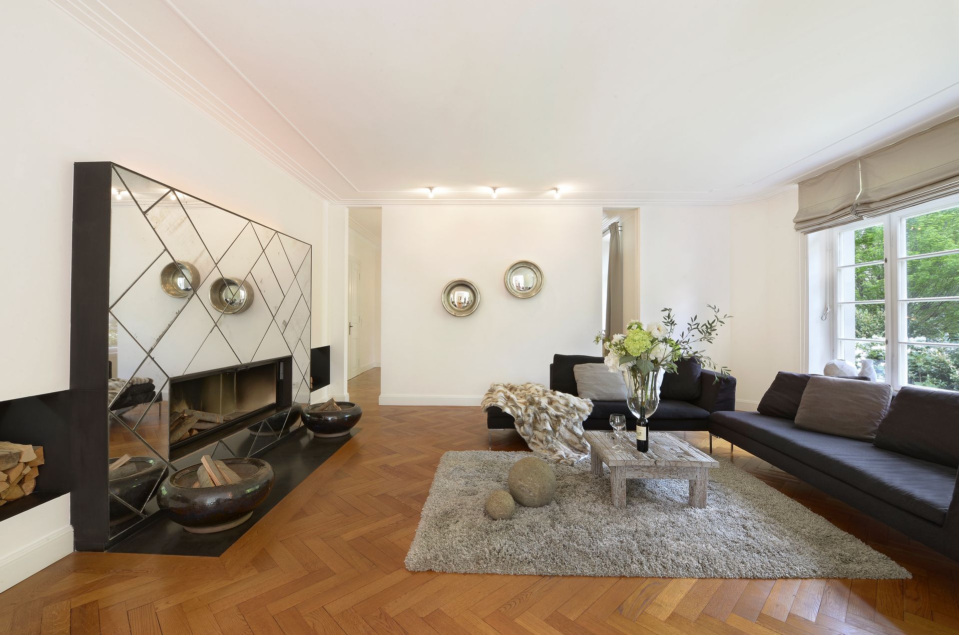 Modern living room with black sofas, fireplace, rug, and large windows.
