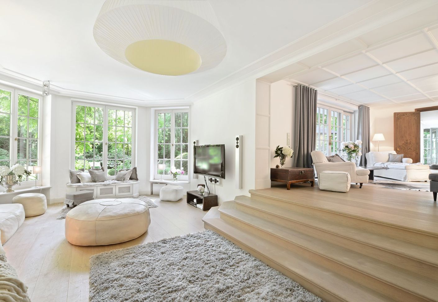 Bright, modern living room with white sofas, large windows, and a step-up seating area