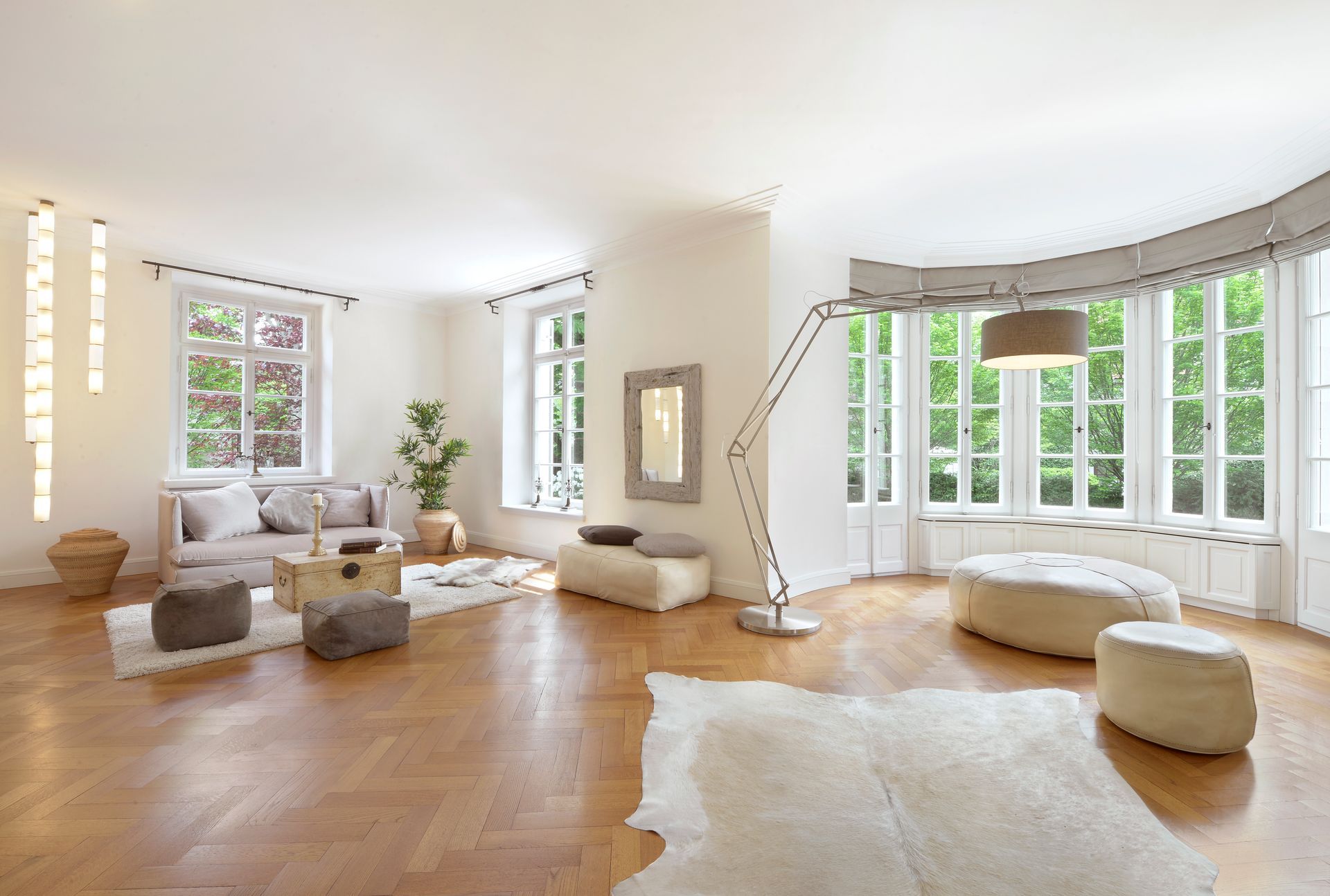 Bright modern living room with white sofas, round ottomans, large windows, and a wood floor