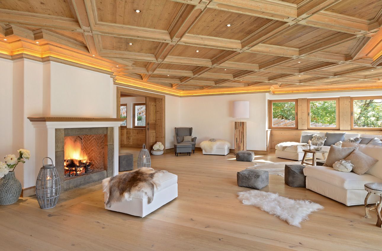 Cozy living room with fireplace, wood ceiling, beige sofas, and large windows overlooking greenery