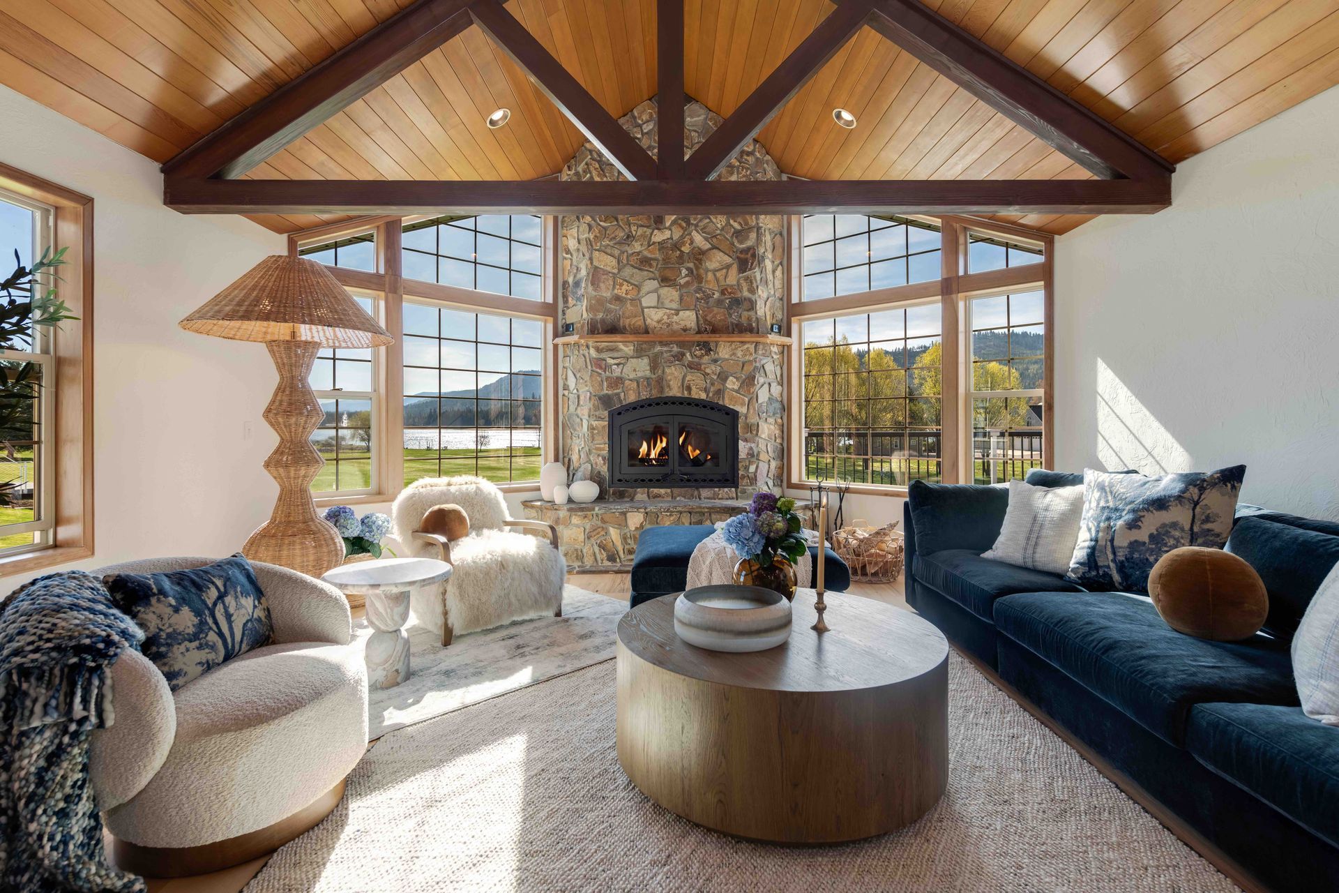 Cozy living room with a stone fireplace, vaulted wood ceiling, and large windows overlooking a view