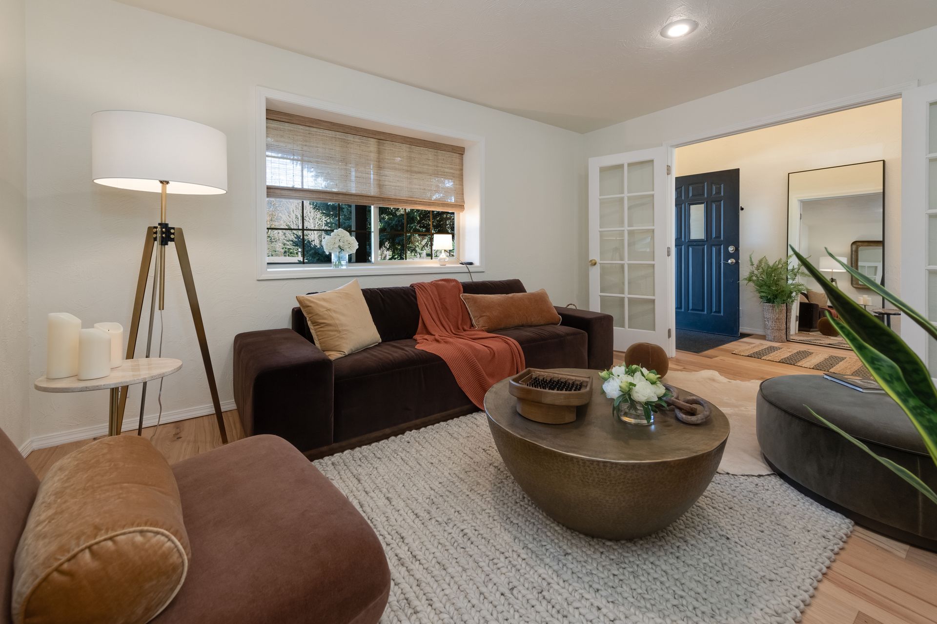 Cozy living room with brown sectional sofa, floor lamp, round coffee table, and blue front door in the entryway