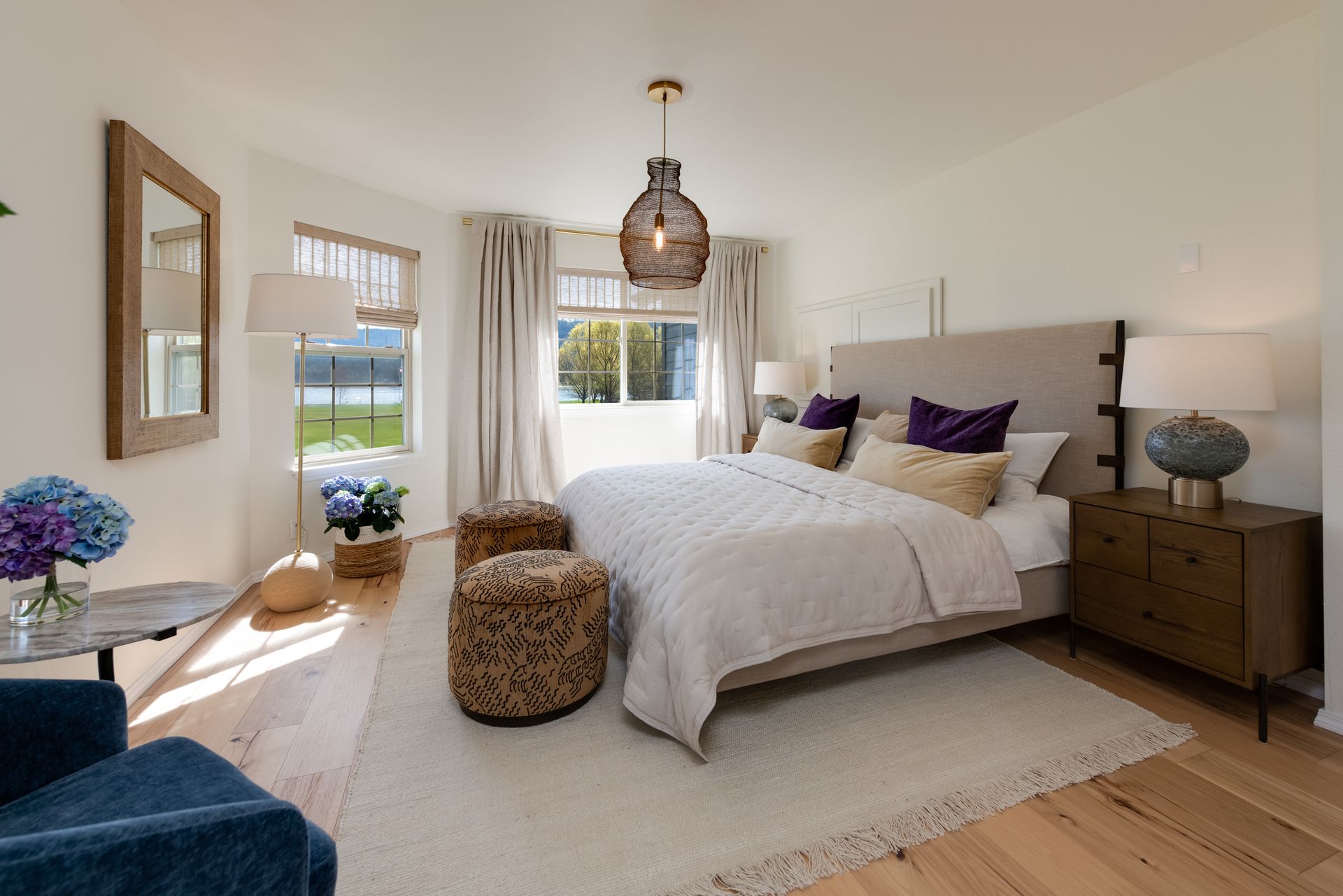 Bright, airy bedroom with a white bed, wooden furniture, pendant light, and large windows overlooking greenery