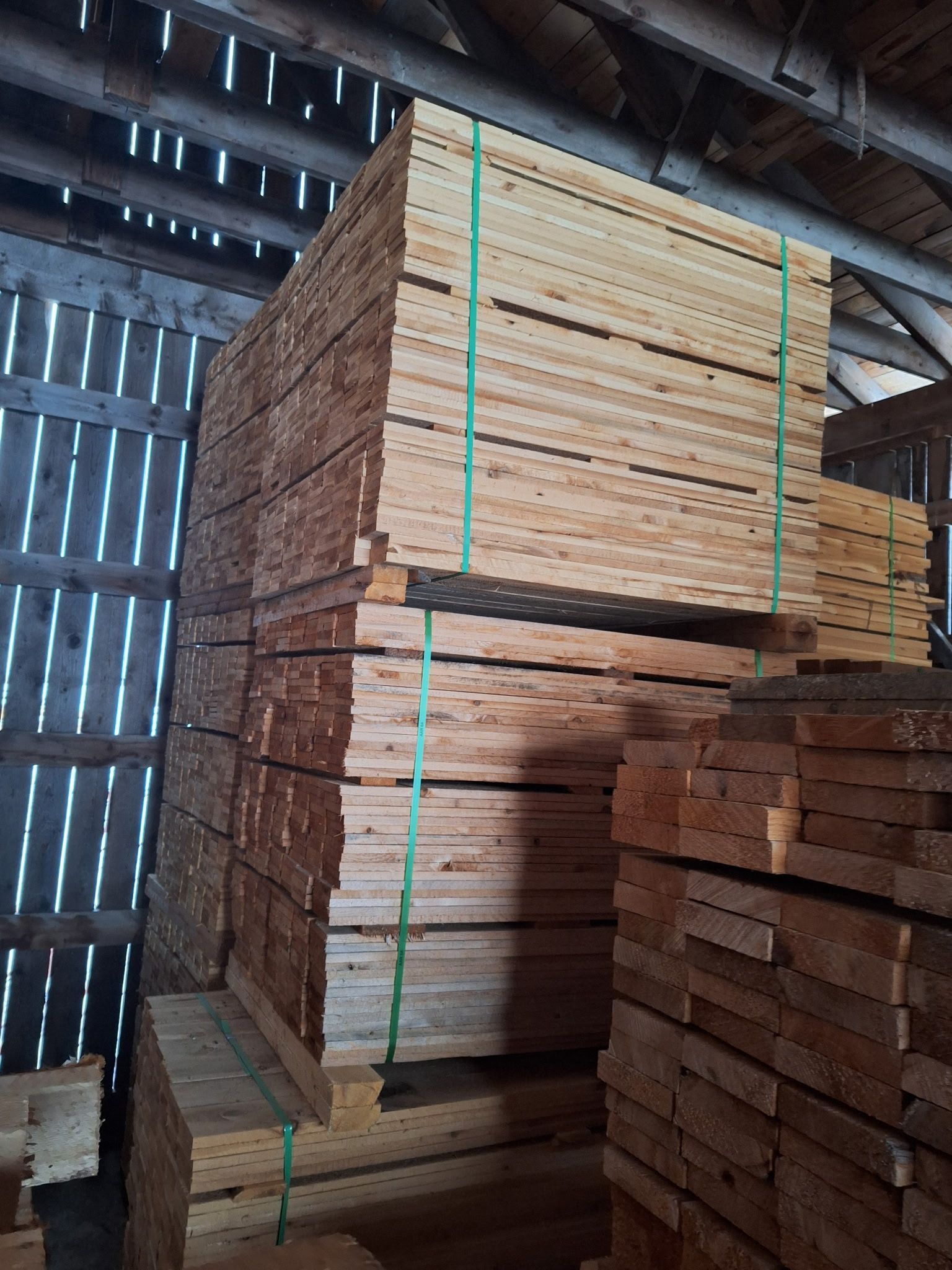 Stack of wooden planks in a barn, secured with green straps.