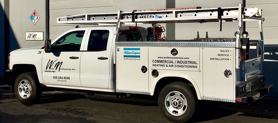 White utility pickup truck with ladder racks and company signage parked outdoors on a street