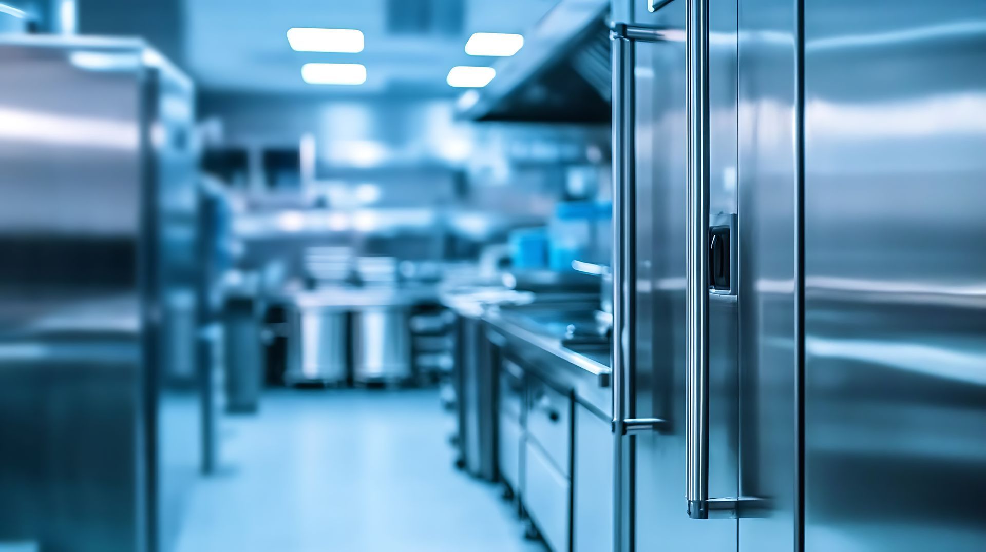 Stainless steel commercial kitchen with blurred appliances and bright overhead lighting