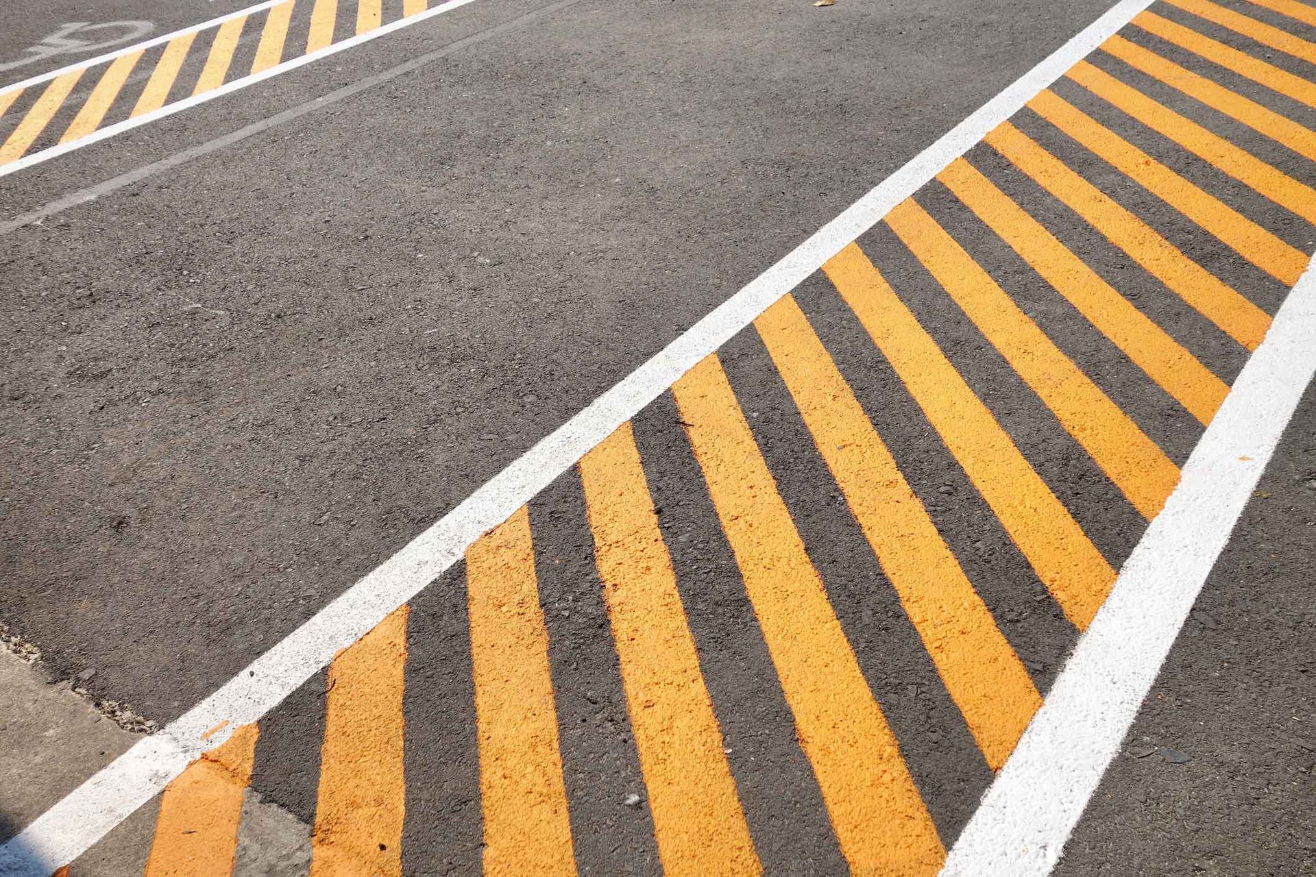 Yellow diagonal road warning stripes and white lane markings painted on asphalt pavement detail view. Yellow diagonal road warning stripes and white lane markings painted on asphalt pavement detail view.