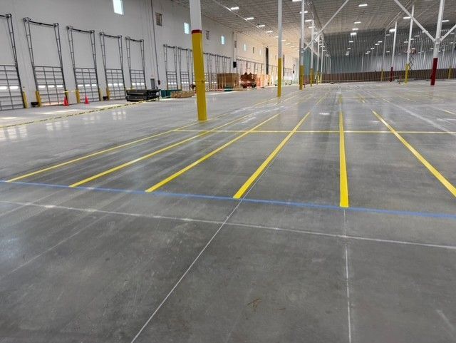 Empty warehouse with yellow floor markings and rows of storage racks under bright lights