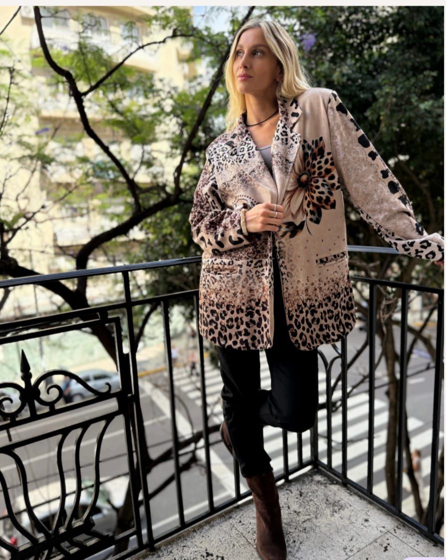 Mujer con chaqueta de estampado de leopardo apoyada en la barandilla de un balcón al aire libre.