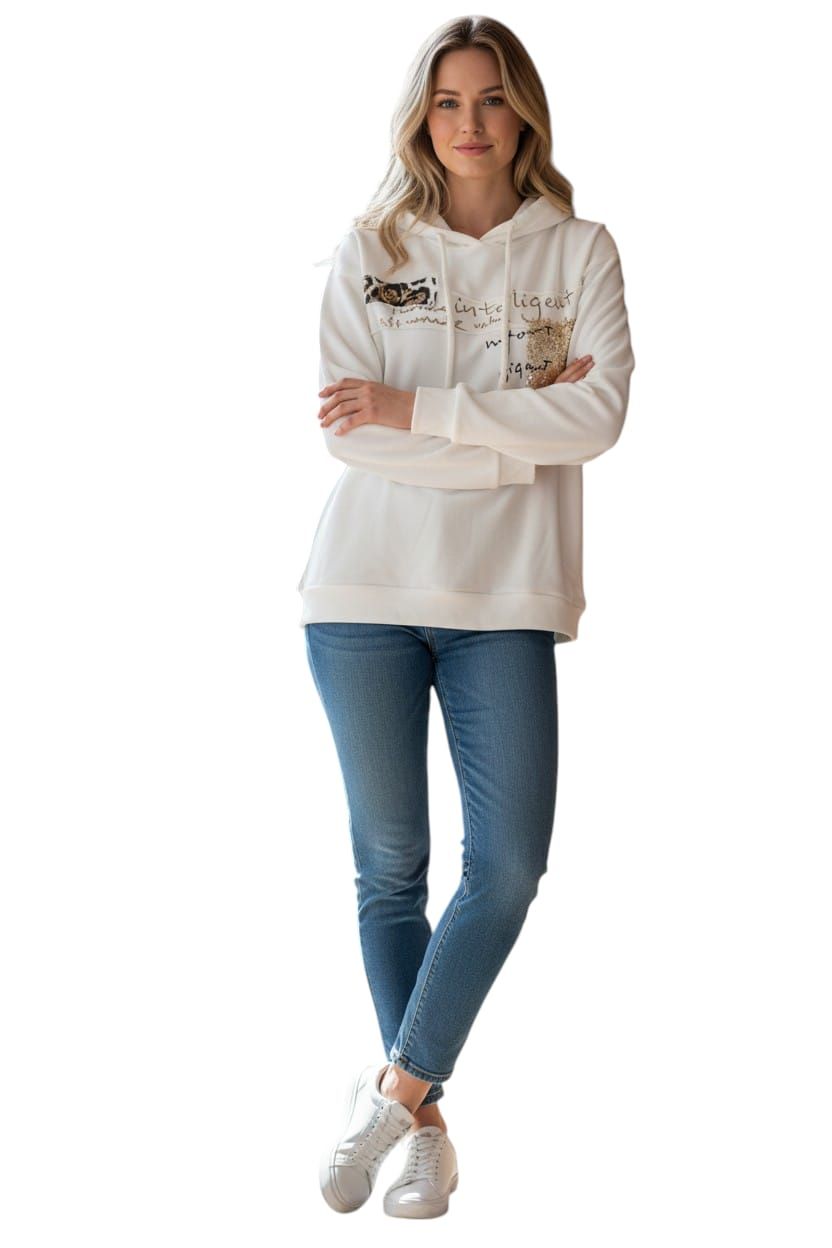 Mujer con sudadera blanca, vaqueros azules y zapatillas blancas de pie con los brazos cruzados sobre un fondo blanco.