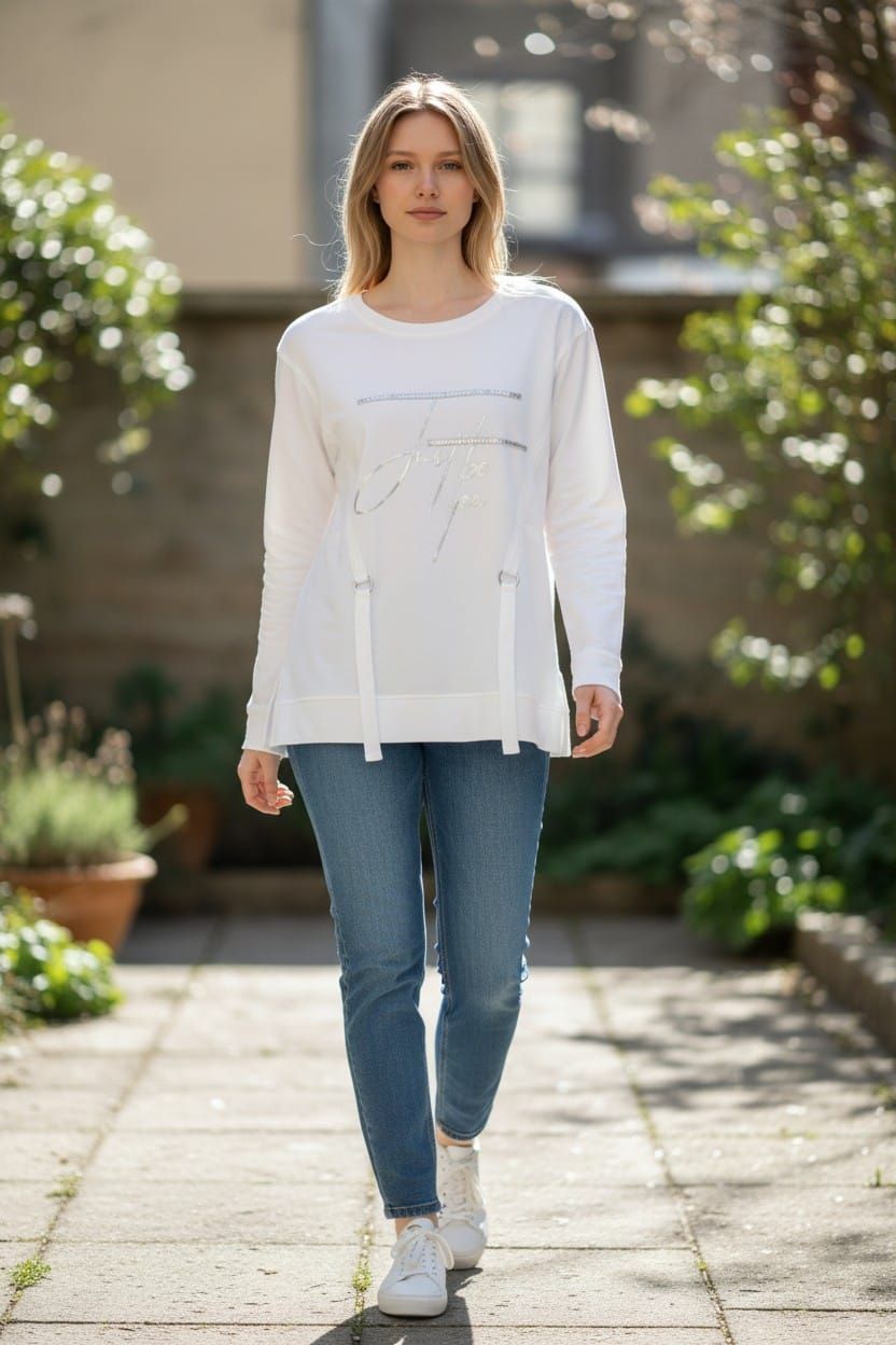 Persona caminando por un sendero soleado de un jardín, vestida con una blusa blanca, vaqueros azules y zapatillas blancas.