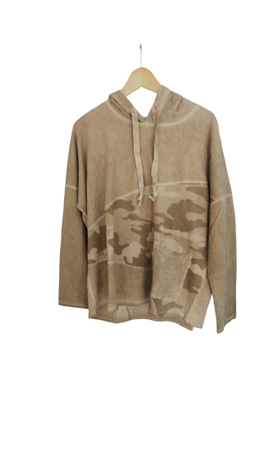 Persona con sudadera beige y vaqueros de pie en el interior de una vivienda, junto a una ventana soleada,