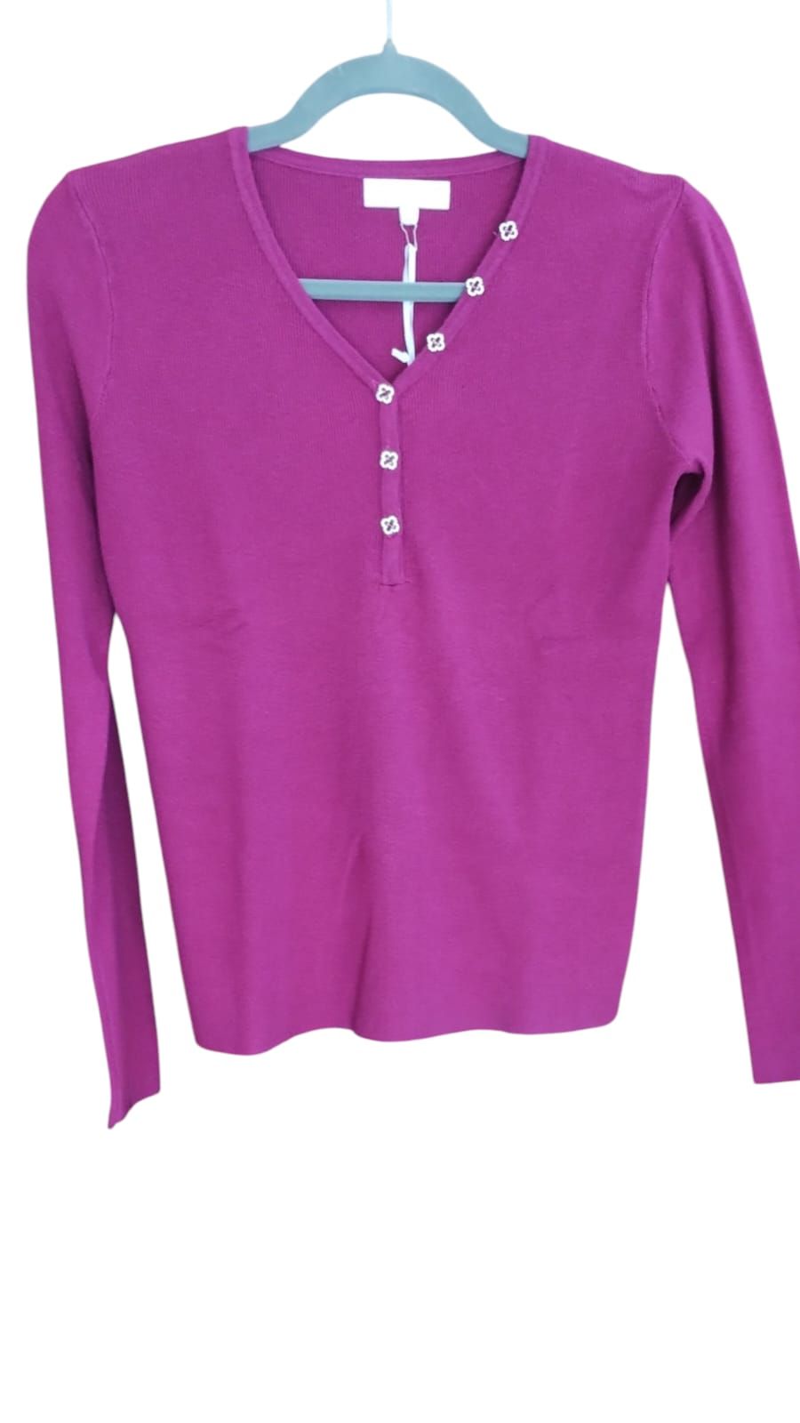 Mujer con blusa magenta y jeans de pie en un loft soleado junto a grandes ventanales.