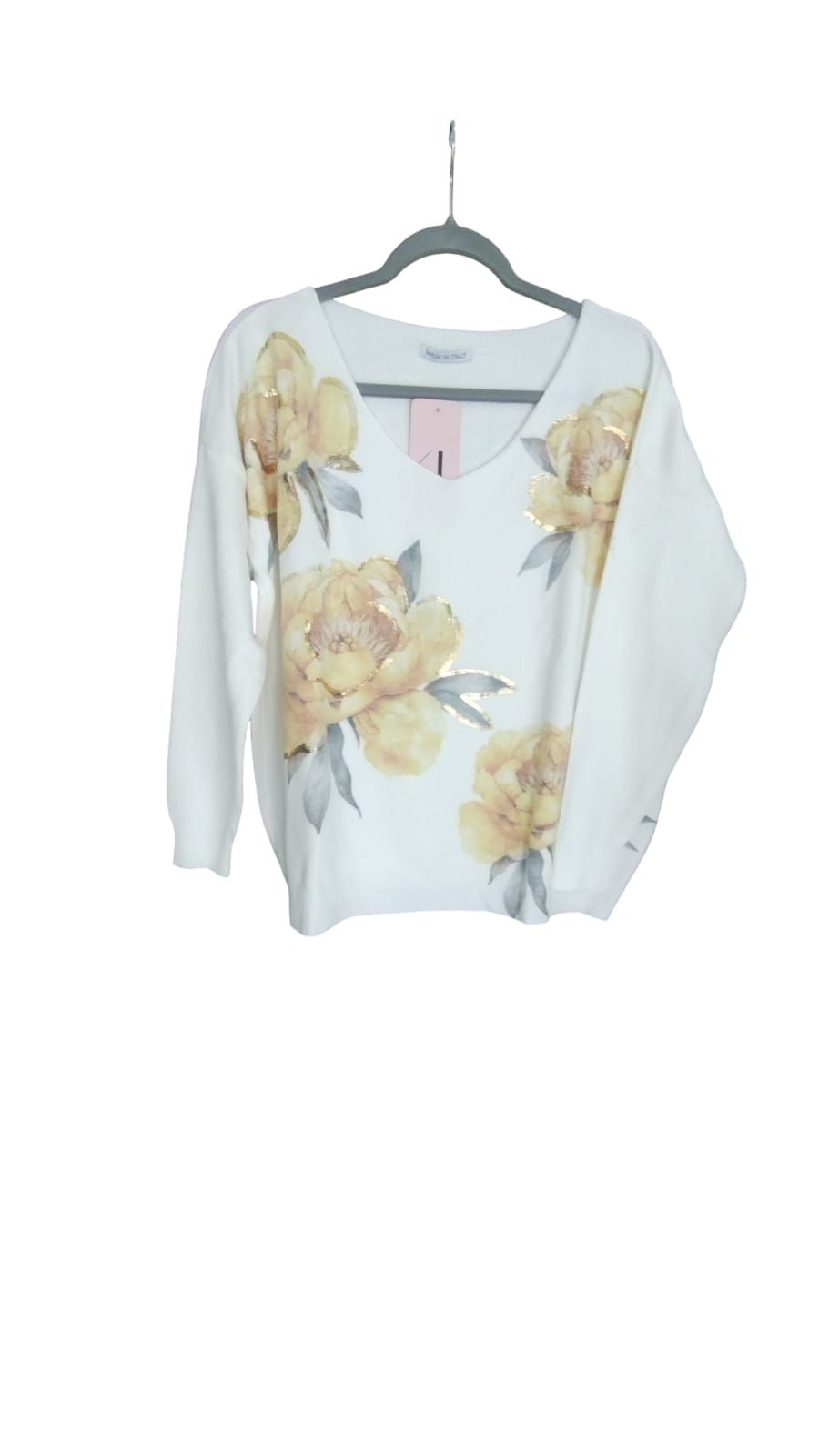 Mujer de pie en una luminosa sala de estar, vestida con una blusa blanca estampada de flores y vaqueros.