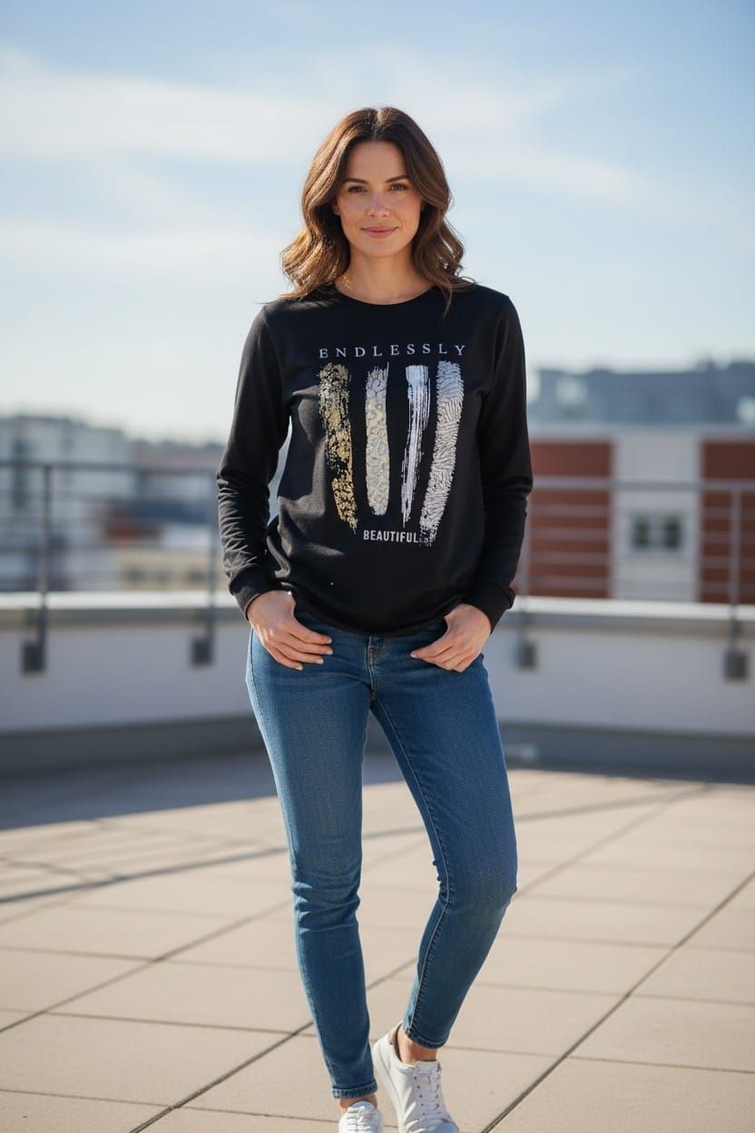 Mujer de pie en una azotea, vestida con vaqueros y una sudadera negra estampada, bajo un cielo azul.