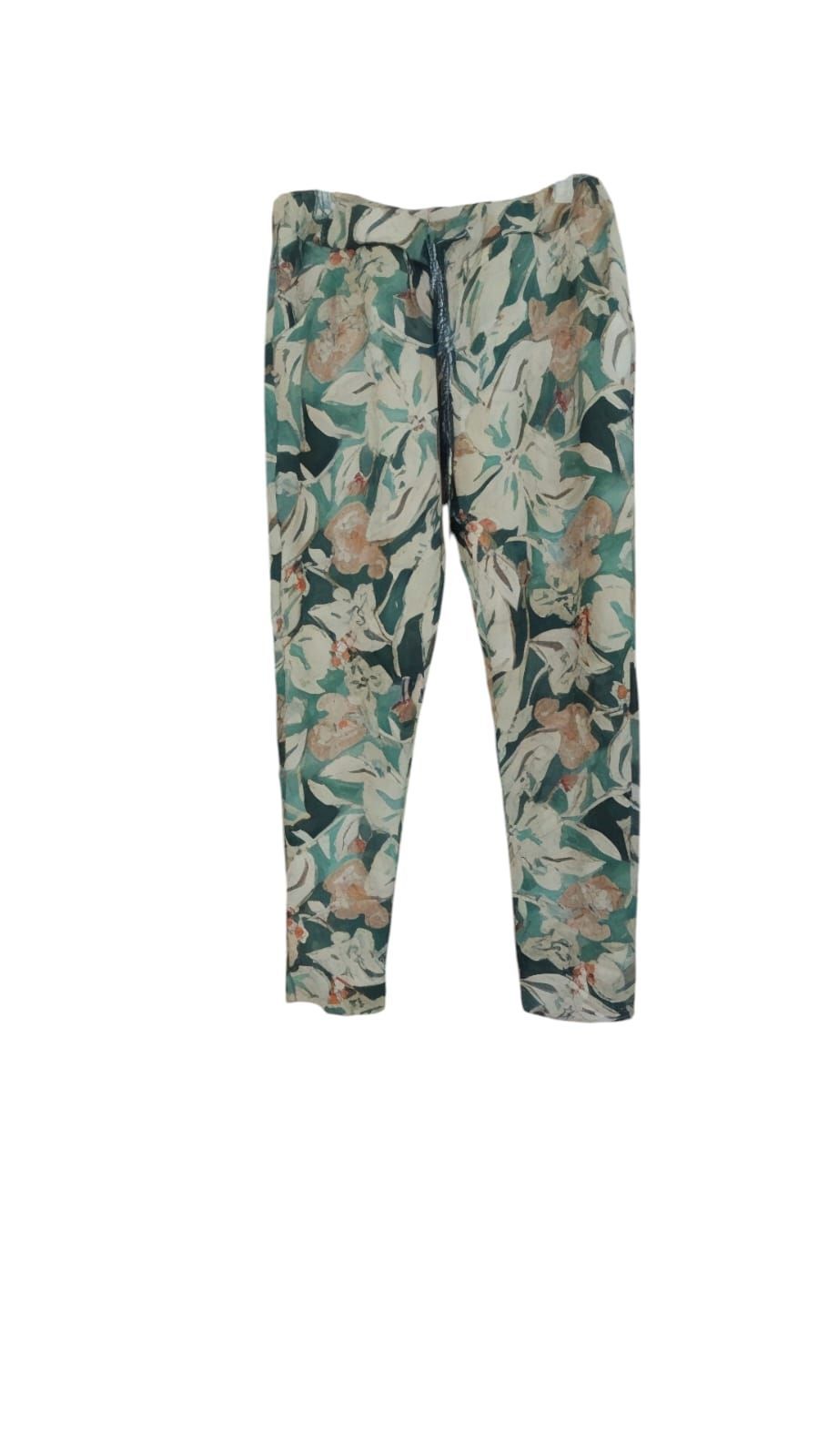 Mujer con blusa marrón y pantalones estampados de flores de pie en un patio soleado con plantas en macetas.
