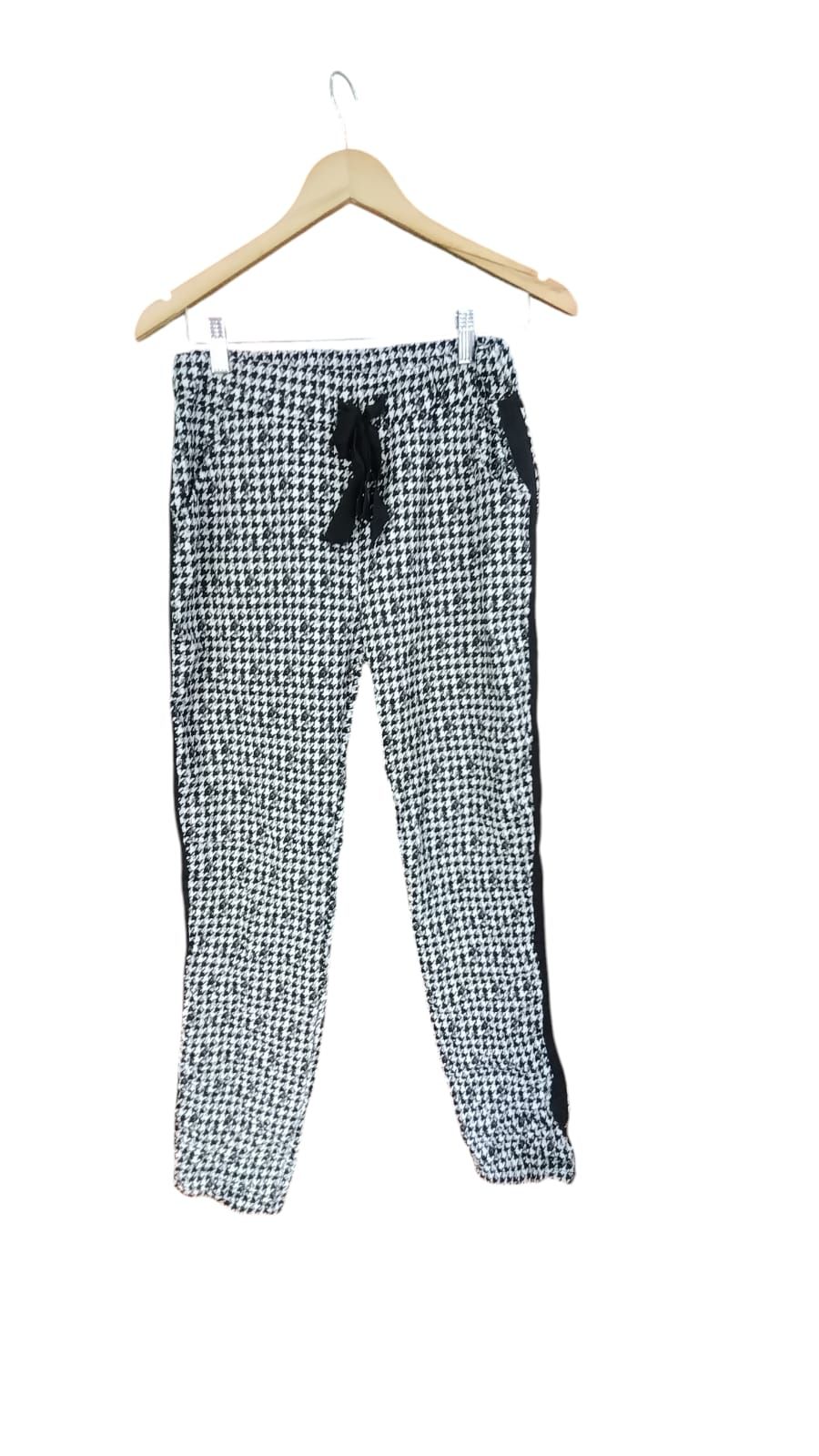 Persona de pie al aire libre en un sendero, vestida con una camiseta negra y pantalones estampados en blanco y negro.