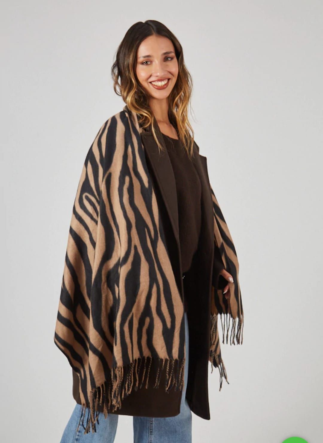 Mujer vestida con un conjunto marrón y un chal de rayas con flecos, sonriendo contra un fondo claro.
