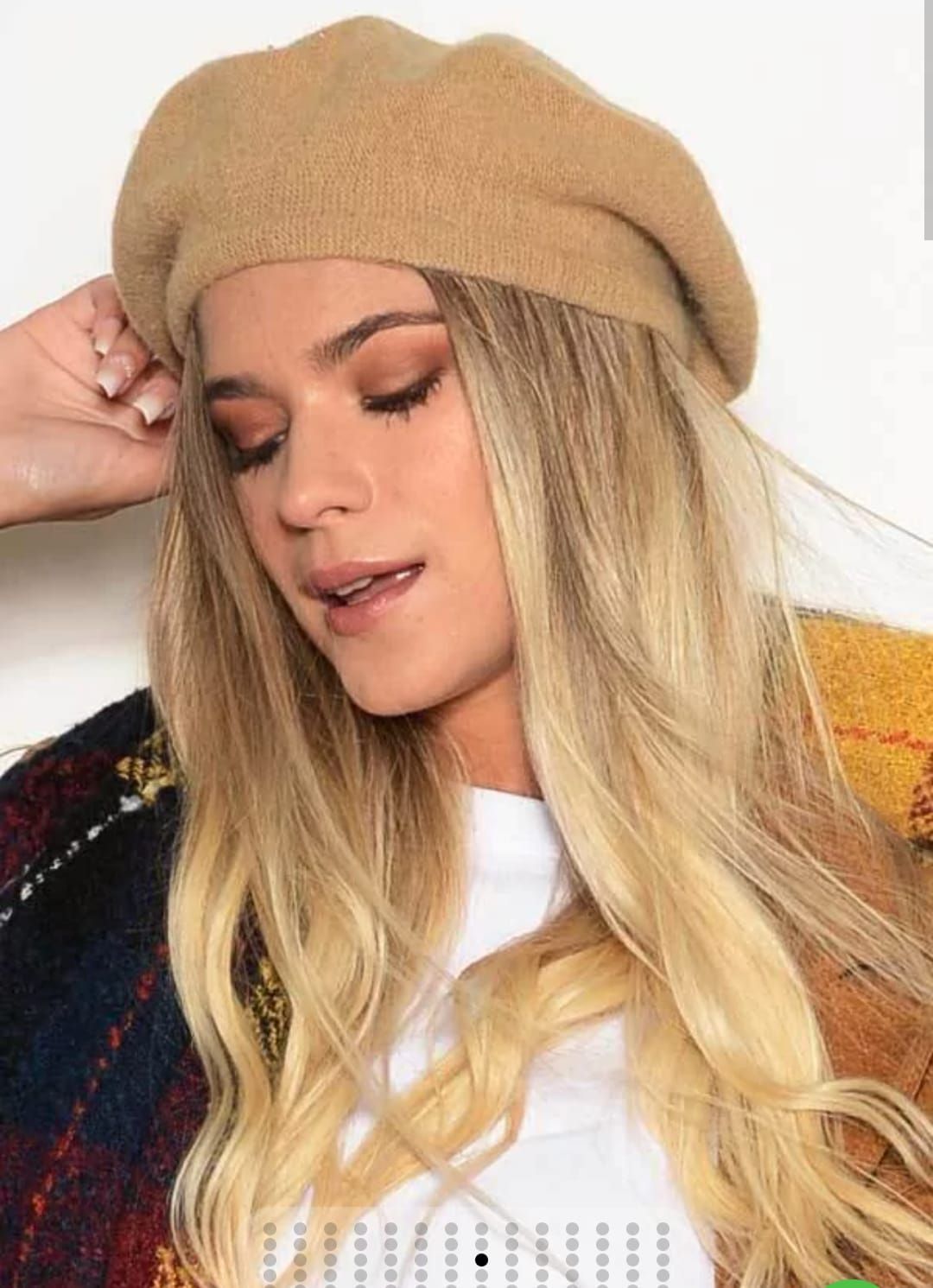 Mujer con boina color canela y cabello rubio, mirando hacia abajo, vestida con camisa blanca y chaqueta colorida.