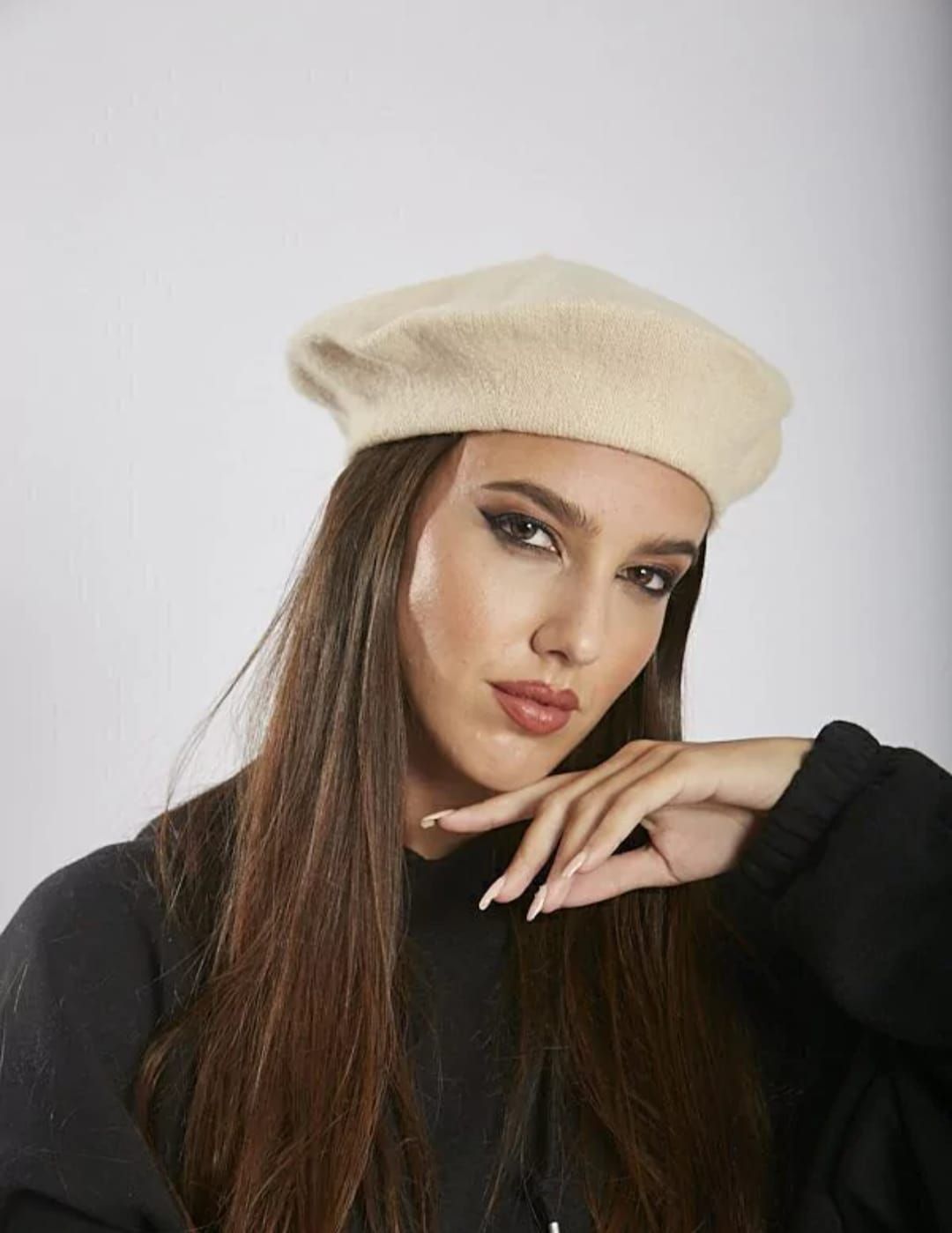 Mujer con boina color canela y cabello rubio, mirando hacia abajo, vestida con camisa blanca y chaqueta colorida.