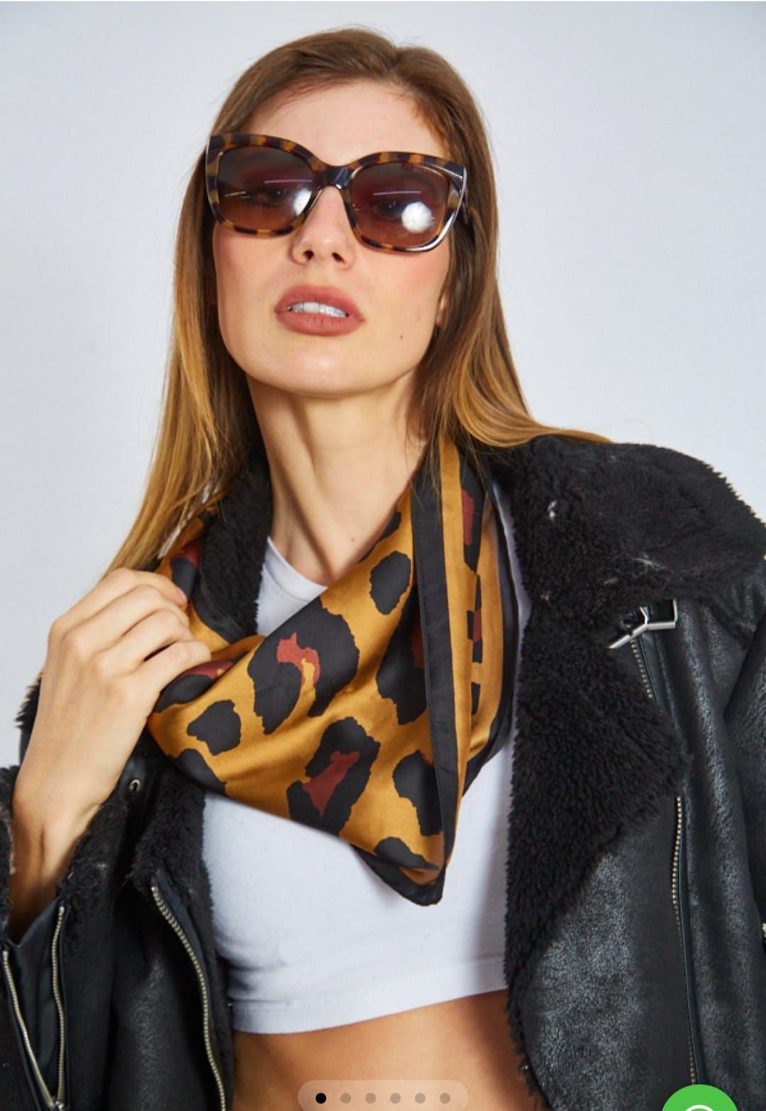 Mujer con gafas de sol y chaqueta negra, sosteniendo una bufanda con estampado de leopardo sobre una blusa blanca.