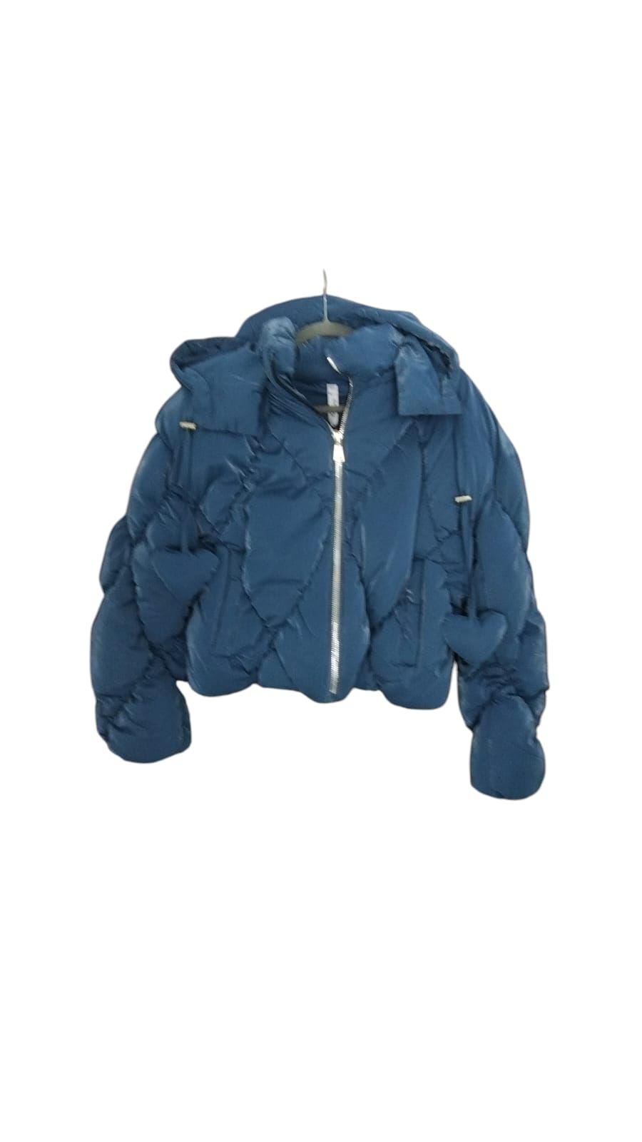 Persona con una chaqueta acolchada azul de pie en un bosque con las manos en los bolsillos.