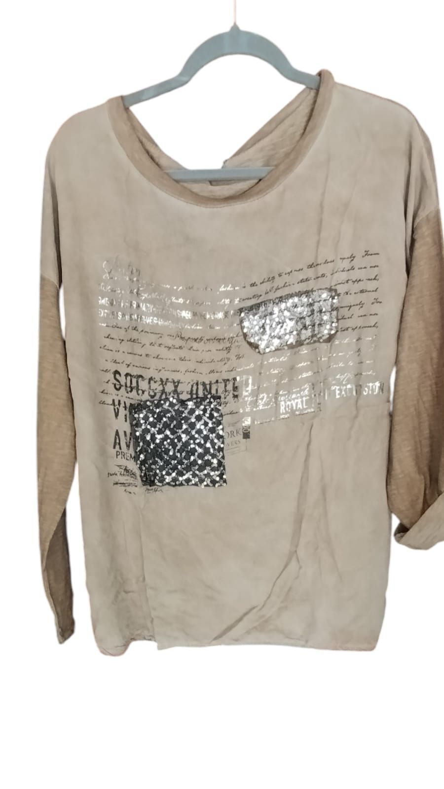 Persona de pie al aire libre en una calle empedrada, vestida con una camiseta beige, vaqueros azules y zapatillas blancas.