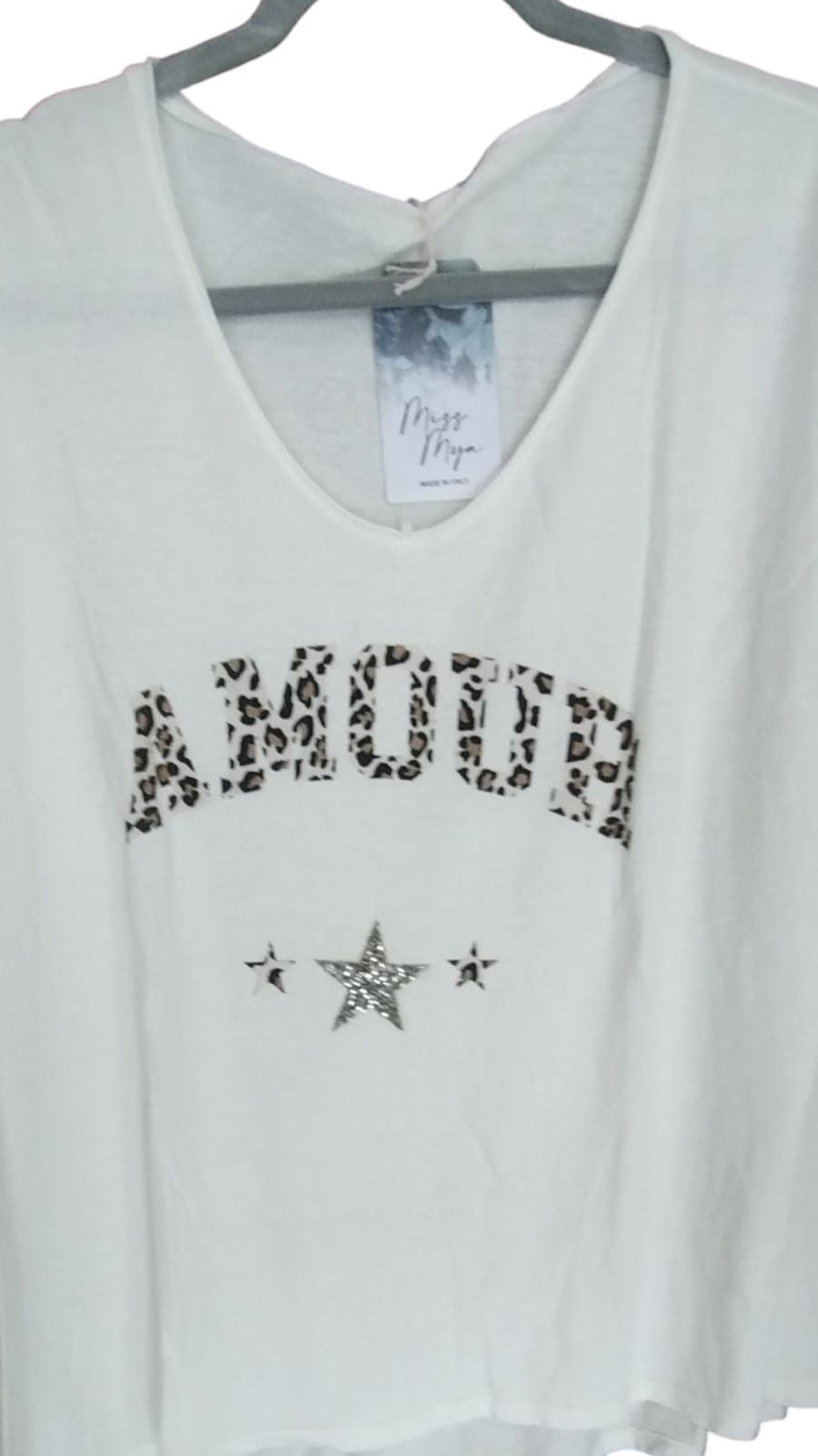 Mujer con sudadera blanca y vaqueros de pie en una habitación soleada con grandes ventanales.