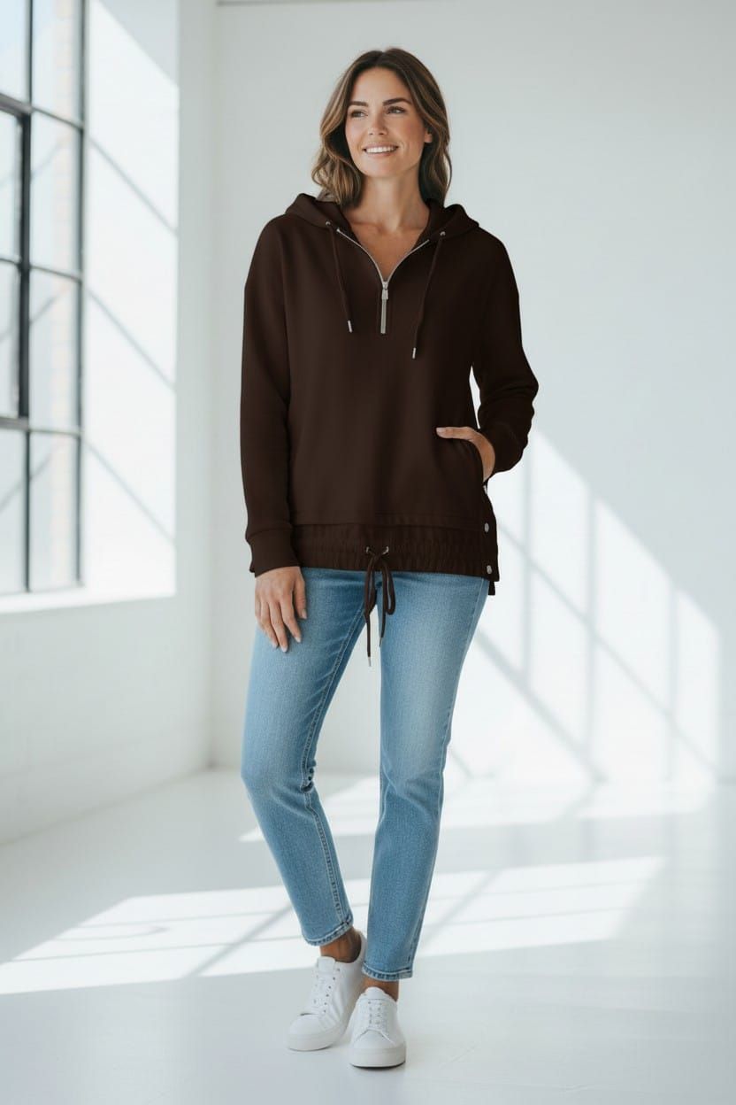 Mujer con blusa blanca y vaqueros de pie en una habitación luminosa y minimalista junto a una gran ventana.