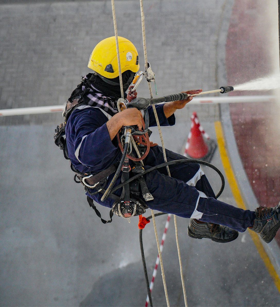 A man wearing a yellow helmet is spraying water from a hose
