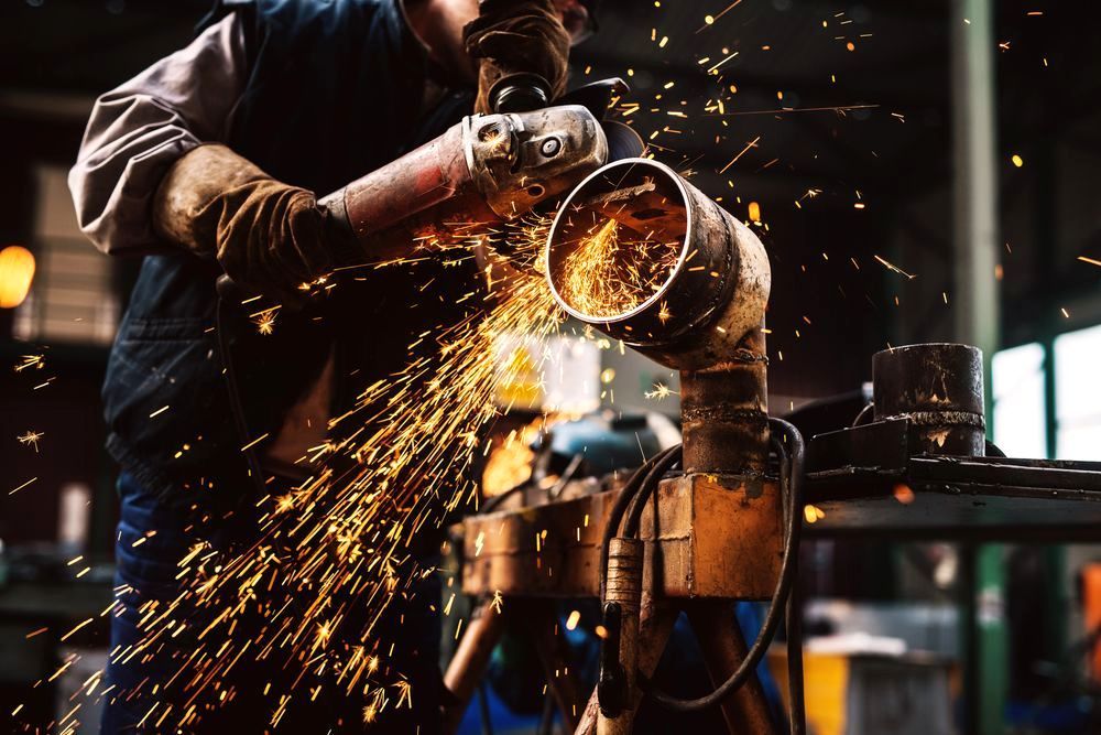 A man is grinding a metal pipe with a grinder in a factory. A man is grinding a metal pipe with a grinder in a factory.