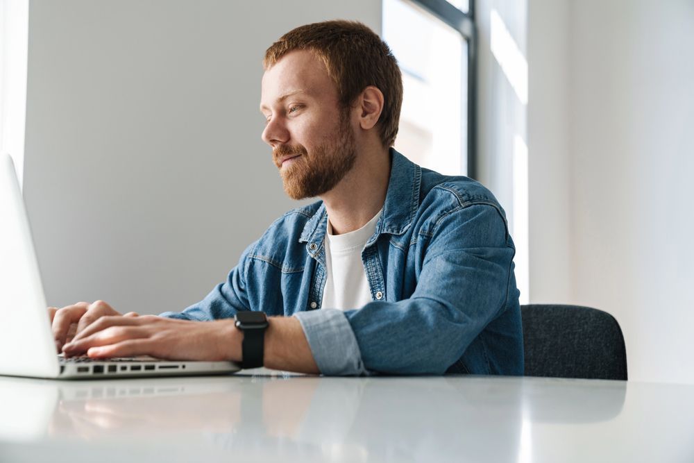 A man is sitting at a table using a laptop computer. A man is sitting at a table using a laptop computer.