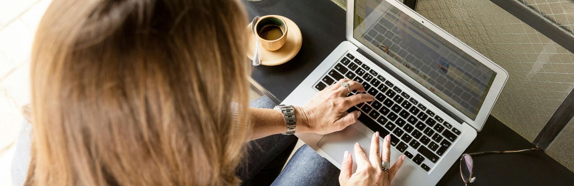 A woman is typing on a laptop computer while sitting at a table with a cup of coffee. A woman is typing on a laptop computer while sitting at a table with a cup of coffee.